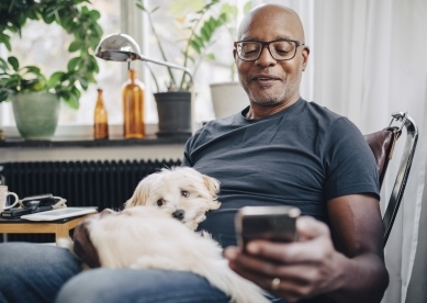 Man looking at cell phone with white dog in his lap